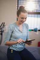 Smiling young female therapist using digital tablet while sitting on bed