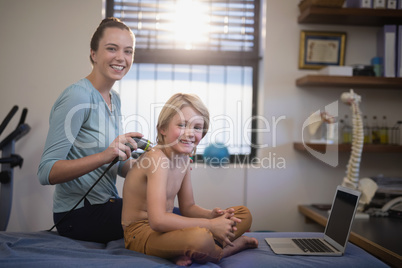 Portrait of smiling female therapist with ultrasound scan and shirtless boy sitting by laptop