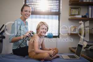 Portrait of smiling female therapist with ultrasound scan and shirtless boy sitting by laptop