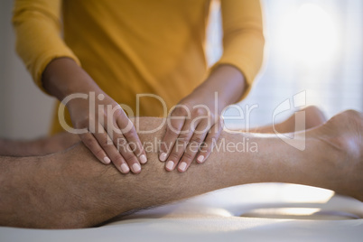 Midsection of female therapist massaging calf of male senior patient lying on bed