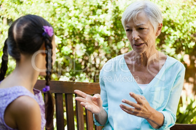 Senior woman talking with granddaughter while sitting on wooden bench