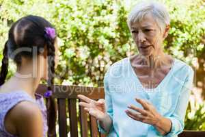 Senior woman talking with granddaughter while sitting on wooden bench