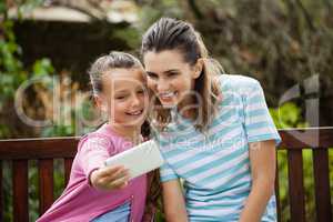 Smiling girl taking selfie with mother sitting on bench