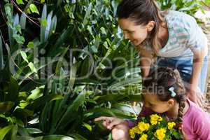 Woman looking while daughter sitting in wheelbarrow pointing towards plants
