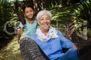 Girl pushing cheerful grandmother sitting in wheelbarrow