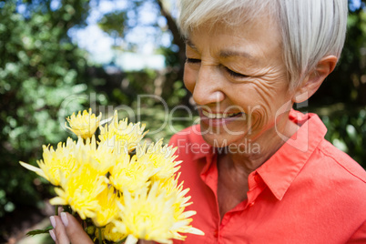 Close-up of smiling senior woman looking at fresh yellow flowers