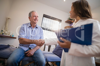 Low angle view of female therapist and senior male patient shaking hands