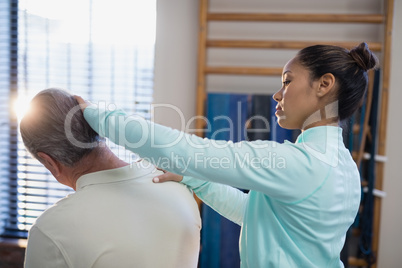 Female therapist examining neck of senior male patient
