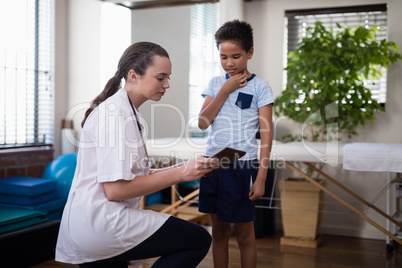 Female therapist kneeling while showing digital tablet to boy