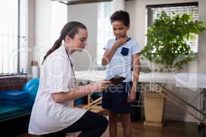 Female therapist kneeling while showing digital tablet to boy