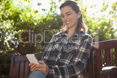 Low angle view of smiling beautiful woman text messaging while sitting on wooden bench