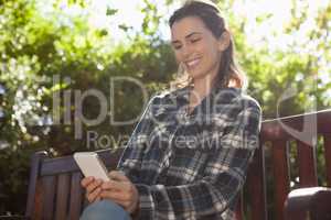 Low angle view of smiling beautiful woman text messaging while sitting on wooden bench