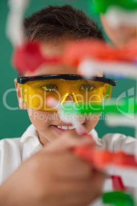 Smiling schoolboy experimenting molecule model in laboratory