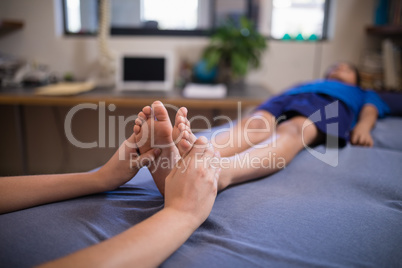 Boy lying on bed while receiving foot massage from female therapist