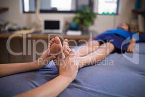Boy lying on bed while receiving foot massage from female therapist