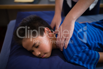 High angle view of boy sleeping on bed while receiving back massage from female therapist
