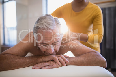 Shirtless male patient lying on bed receiving neck massage from young female therapist