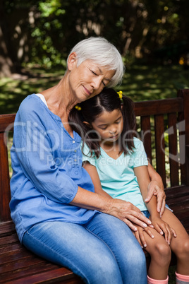 Granddaughter and grandmother sleeping while sitting on wooden bench