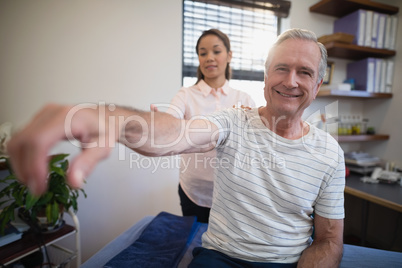 Portrait of smiling senior male patient sitting with female doctor examining shoulder