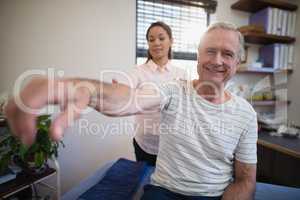 Portrait of smiling senior male patient sitting with female doctor examining shoulder