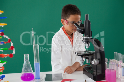 Smiling schoolboy looking through microscope in laboratory