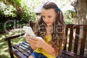 Girl using cellphone while sitting on wooden bench