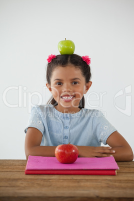 Schoolgirl sitting with green apple on her head against white background