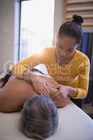 Shirtless patient lying on bed receiving neck massage from female therapist