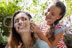 Smiling girl positioning white flower in hair of mother