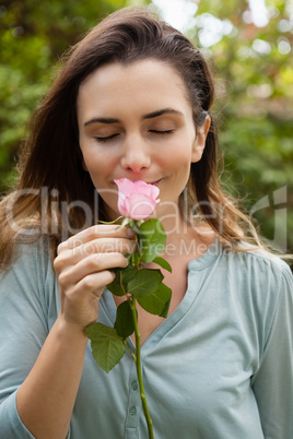 Beautiful woman with eyes closed smelling pink rose