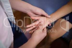 Midsection of female therapist massaging palm with boy sitting on bed