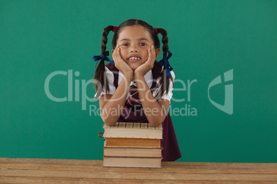 Schoolgirl leaning on books stack against chalkboard in classroom