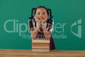 Schoolgirl leaning on books stack against chalkboard in classroom