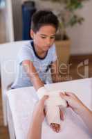 Female therapist wrapping bandage on hand of boy sitting at table