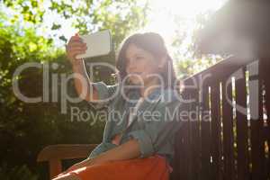 Girl taking selfie from mobile phone while sitting on bench during sunny day