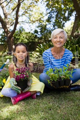 Portrait of smiling granddaughter and grandmother holding plants sitting with crossed legs