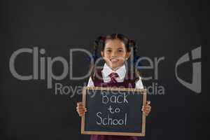 Portrait of schoolgirl holding slate with text against blackboard