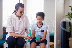 Female therapist sitting by boy on chairs with squeeze balls
