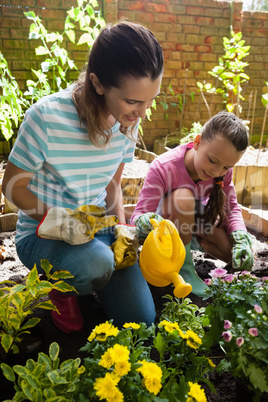 Smiling mother kneeling by girl watering plants