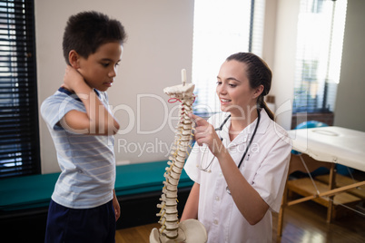 Female therapist pointing at artificial spine while explaining to boy