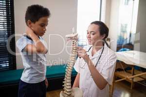 Female therapist pointing at artificial spine while explaining to boy
