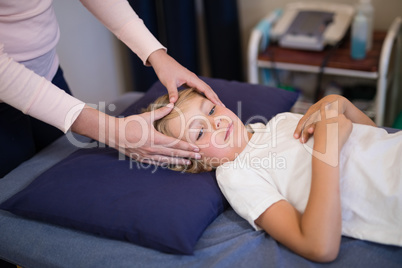 Female therapist massaging head of boy lying on bed