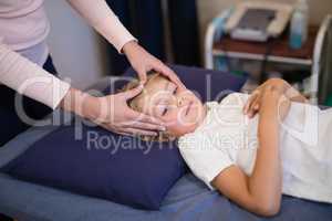 Female therapist massaging head of boy lying on bed