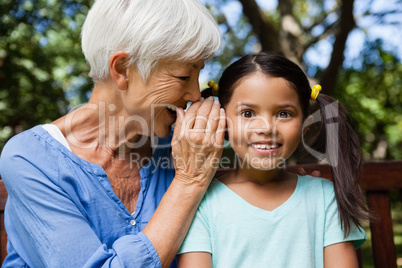 Smiling grandmother whispering in ears of girl