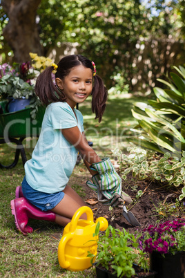 Portrait of smiling girl kneeling while digging soil with trowel