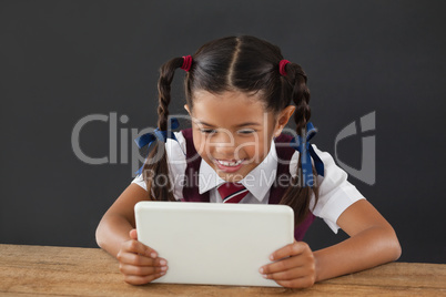 Schoolgirl using digital tablet against blackboard