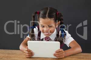 Schoolgirl using digital tablet against blackboard