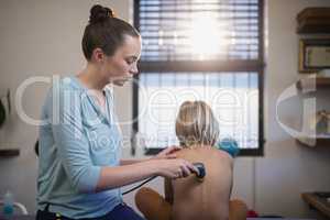 Female therapist using ultrasound machine on back of shirtless boy
