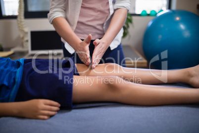 Young female therapist massaging knee of boy lying on bed