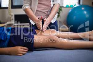 Young female therapist massaging knee of boy lying on bed